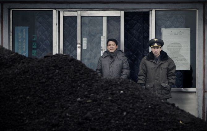 Un officier nord-coréen (à dr.) avec un compatriote derrière un amas de charbon sur les rives du fleuve Yalu dans la ville frontalière nord-coréenne de Siniuju, le 14 décembre 2012. Le 18 février 2017, le ministère du Commerce chinois annonce la suspension de toutes les importations de charbon nord-coréen. (Wang Zhao / AFP / Getty Images)