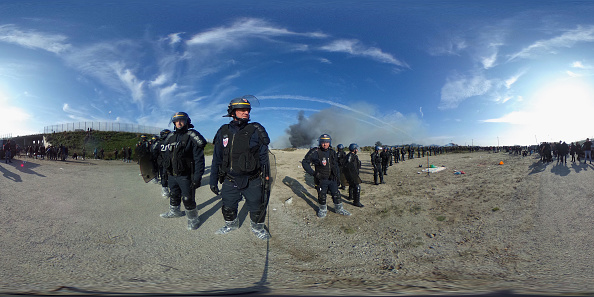 Image panoramique à 360 degrés.
Des CRS face à des migrants de la jungle. Depuis le démantèlement il y a un an de la "Jungle", le gigantesque bidonville abritant 7.000 migrants de Calais, des centaines de migrants sont revenus sur le territoire de cette ville portuaire située à l'entrée du tunnel sous la Manche, espérant gagner l'Angleterre.
(Christopher Furlong / Getty Images)