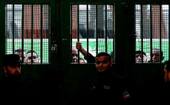Les forces de sécurité fidèles au Hamas montent la garde alors que les Palestiniens attendent devant un poste de fortune à Khan Younis dans le sud de Gaza le 18 novembre 2017, attendant l'autorisation de prendre un bus pour traverser le poste frontalier de Rafah avec l'Egypte, après trois jours d'ouverture. la première fois depuis l'accord de réconciliation palestinien. Seules les affaires humanitaires enregistrées auprès du ministère palestinien de l'Intérieur seraient autorisées à quitter le passage, ce qui inclurait jusqu'à 20 000 personnes dans l'enclave appauvrie de deux millions d'habitants. L'accord de réconciliation palestinien négocié par l'Egypte devrait conduire à une ouverture plus régulière du point de passage de Rafah, qui était totalement scellé depuis août 2017, et a été fermé par le Caire pendant des années auparavant. 
(MAHMUD HAMS / AFP / Getty Images)