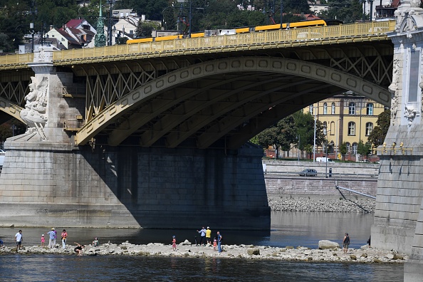 -Les gens marchent sur une partie sèche du Danube près du pont Margaret à Budapest. La capitale hongroise a battue du temps chaud des dernières semaines. l le niveau exceptionnellement bas des eaux du fleuve, a permis la découverte d’un trésor. Photo ATTILA KISBENEDEK / AFP / Getty Images.