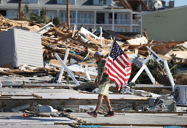 Un homme porte un drapeau américain qu'il a trouvé en marchant sur les fondations de maisons démolies par l'ouragan Michael qui a traversé la région le 12 octobre 2018 à Mexico Beach, en Floride. L'ouragan a frappé la zone des manches avec des vents de catégorie 4 causant des dégâts importants. (Photo : Joe Raedle/Getty Images)