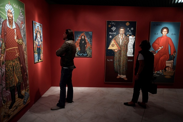 -Les visiteurs regardent des portraits d'écrivains célèbres, de stars du rock et de politiciens à la manière d'icônes religieuses réalisées par l'artiste grec Gigas lors de la conférence de presse de la Biennale d'Athènes 2018 le 25 octobre 2018. Photo LOUISA GOULIAMAKI/AFP/Getty Images.