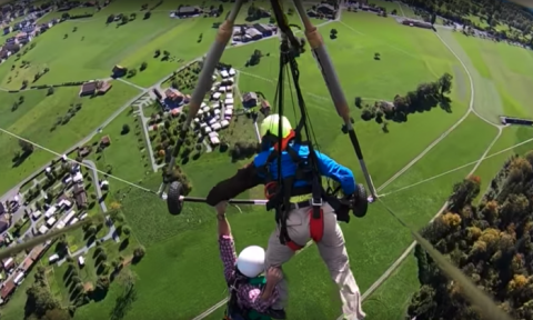 Le Youtuber Chris Gursky est suspendu à la barre du deltaplane et à la jambe de son pilote au-dessus de la campagne suisse en octobre 2018. (Screengrab/YouTube/Chris Gursky)