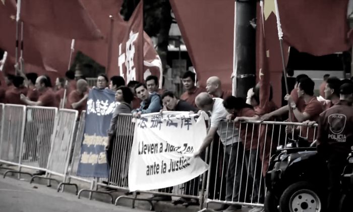 Neuf pratiquants argentins de Falun Gong accrochent deux banderoles sur les barrières de contrôle de la foule, qui disent "Mettez fin à la persécution du Falun Gong" et "Traduisez Jiang Zemin en justice" en espagnol et chinois. Les pratiquants sont entourés de partisans du Parti communiste chinois envoyés pour accueillir le dirigeant chinois Xi Jinping. (Capture d'écran via YouTube)