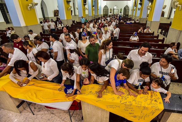 -Le 22 février 2019, les partisans du chef de l'opposition vénézuélienne Juan Guaido signent un drapeau vénézuélien lors d'une réunion à la cathédrale du très saint Rosaire à Willemstad, Curaçao, Antilles néerlandaises.. Photo de Luis ACOSTA / AFP / Getty Images.