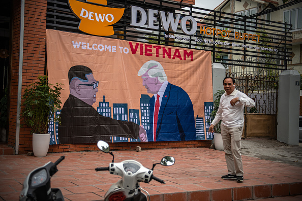 -Un homme s'arrête devant une banderole montrant le président américain Donald Trump et le dirigeant nord-coréen Kim Jong-un se serrant la main à côté des mots « Bienvenue au Vietnam » accrochés en face de l'hôtel Marriott où le président Trump devrait rester pendant prochain sommet, le 25 février 2019 à Hanoi, au Vietnam. Photo by Carl Court/Getty Images.