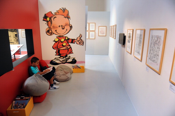 -Un enfant lit un livre à côté de dessins et de pages de couverture de Spirou présenté lors de l'exposition '' Spirou, un héros dynamique '' au cite international de la bande dessinée à Angoulême, en juillet 9, 2013. Photo MEHDI FEDOUACH/AFP/Getty Images.