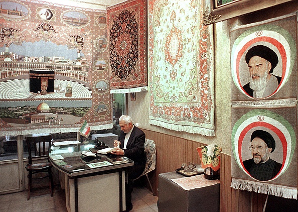 -Un Iranien attend un client dans son magasin de tapis, le 10 novembre au bazar de Téhéran. L’Iran est un important exportateur de tapis et l’industrie est la deuxième source de devises du pays. Un tapis avec les portraits du défunt chef suprême Ayatollah Ruhollah Khomeiny et de l'actuel président Mohamad Khatami. Photo ATTA KENARE / AFP / Getty Images.