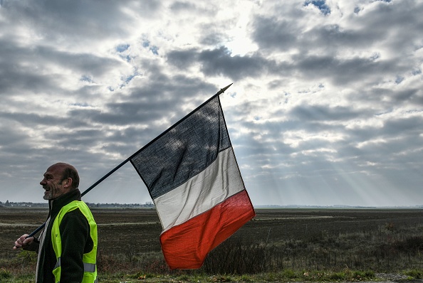 "Gilets jaunes", un homme tient un drapeau français alors qu'il participe à un barrage routier le 17 novembre 2018 à Dole, dans l'est de la France. (Photo : SEBASTIEN BOZON/AFP/Getty Images)