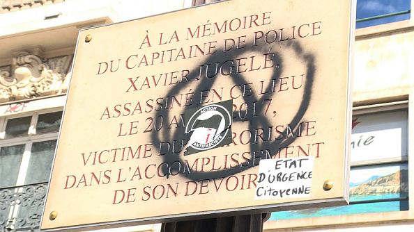 Plaque commémorative dédiée au policier français Xavier Jugele, tué par un djihadiste lors d'une attaque sur l'avenue des Champs-Elysées le 20 avril 2017, portant un symbole anarchiste,lors du 18e samedi consécutif de manifestations organisées par le mouvement " gilets jaunes ". (Photo : MYRIAM ADAM/AFP/Getty Images)