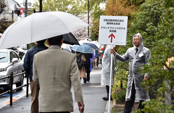 -Un employé de Nissan Motor tient une affiche sur un trottoir pour guider les actionnaires arrivés vers un hôtel où la réunion extraordinaire des actionnaires de la société se tiendra à Tokyo le 8 avril 2019. Photo de Kazuhiro NOGI / AFP / Getty Images.