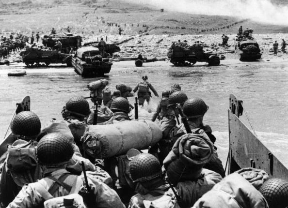 -Juin 1944 : Des troupes d'assaut américaines et du matériel débarquent sur la plage d'Omaha, sur la côte nord de la France, la fumée à l'arrière-plan provient de tirs navals soutenant l'attaque. Photo Fox / Hulton Archive / Getty Images.