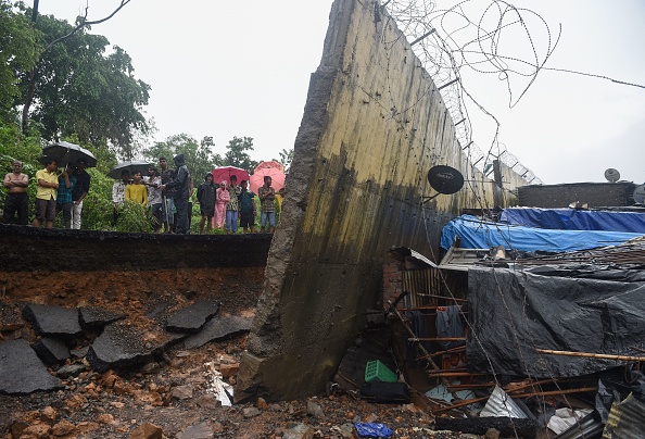 -Des spectateurs se tiennent derrière une partie du mur brisé qui s'est effondré à Mumbai le 2 juillet 2019. Au moins 15 personnes ont été tuées dans la capitale financière de l'Inde, lorsqu'un mur s'est effondré lors des pluies torrentielles de la mousson. Photo de PUNIT PARANJPE / AFP / Getty Images.