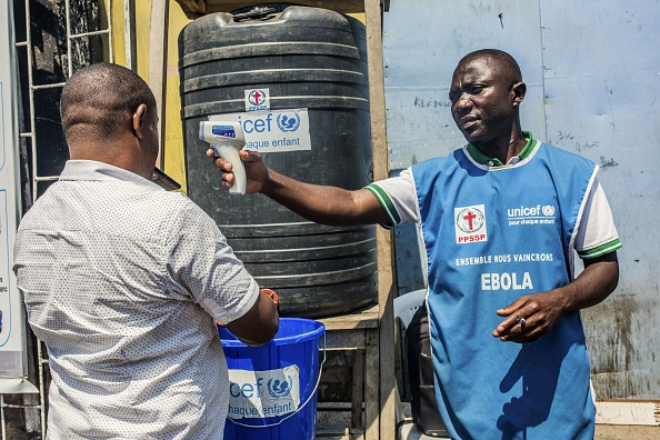 -Un homme se lave les mains au chlore alors qu’un agent de santé de l’Unicef tient un thermomètre dans une station de lavage le 15 juillet 2019 à Goma. Les autorités de la République démocratique du Congo ont appelé au calme après qu'un prédicateur soit tombé malade du virus Ebola à Goma, dans l'est du pays, premier cas enregistré de la maladie dans le centre urbain de la région. Photo par Pamela TULIZO / AFP / Getty Images.