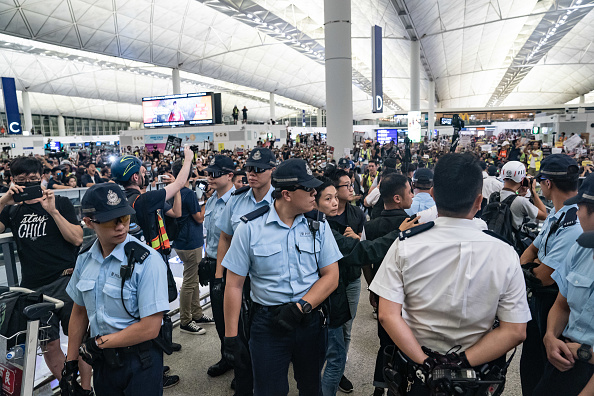 -Des policiers se tiennent avec des manifestants à l'aéroport international de Hong Kong lors d'une manifestation le 13 août 2019 à Hong Kong, Chine. Photo par Anthony Kwan / Getty Images.