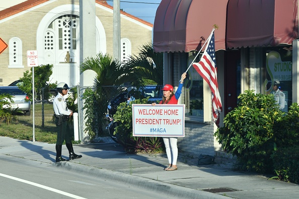 -Un supporter porte des pancartes et un drapeau pour accueillir le président Trump à son arrivée à West Palm Beach, en Floride, le 18 avril 2019. Photo de Nicholas Kamm / AFP via Getty Images.