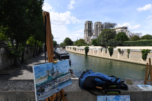 -Cette photo prise le 13 juillet 2019 montre une peinture représentant Notre-Dame de Paris avant qu'elle ne soit gravement endommagée par un énorme incendie en avril dernier et que Notre-Dame de Paris d'origine soit reconstruite en arrière-plan. Photo par ALAIN JOCARD / AFP / Getty Images.
