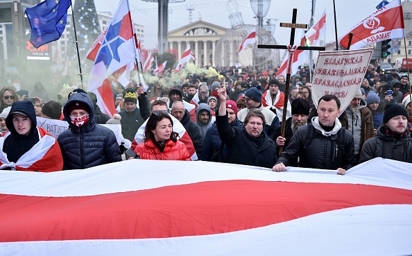 -Des gens portent un drapeau géorgien historique blanc-rouge-blanc géant et des bannières anti-intégration alors qu'ils assistent à un rassemblement de l'opposition contre un projet d'intégration biélorusse-russe à Minsk, le 7 décembre 2019. « Ce n’est pas de l'intégration, c'est une occupation » et "le président vend notre pays". Photo de SERGEI GAPON / AFP via Getty Images.