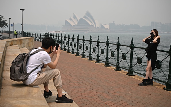 -Les touristes portant des masques prennent des photos, l'Opéra à l’arrière est enveloppé de brume causée par des feux de brousse à proximité, à Sydney le 10 décembre 2019. Une brume toxique a recouvert Sydney le 10 décembre. Photo de PETER PARKS / AFP via Getty Images.