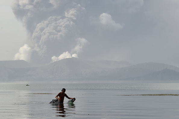 -Un pêcheur patauge avec ses filets dans les eaux du lac Taal alors que le volcan Taal crache des cendres depuis la ville de Tanauan dans la province de Batangas, au sud de Manille, le 13 janvier 2020. Photo de TED ALJIBE / AFP via Getty Images