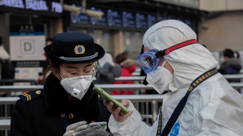 Un membre du personnel de sécurité portant des vêtements de protection pour aider à stopper la propagation du virus mortel apparu à Wuhan, s'entretient avec un employé du métro (g) portant un masque à l'entrée d'une station de métro à Pékin le 27 janvier 2020. (Nicolas Asfouri/AFP via Getty Images)