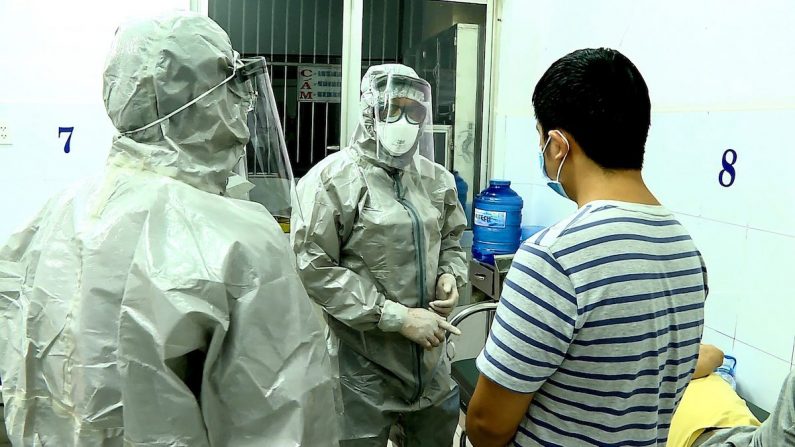  Le personnel médical portant des combinaisons de protection interagit avec deux patients (au lit et debout) diagnostiqués porteurs du coronavirus dans une chambre d'isolement de l'hôpital Cho Ray à Ho Chi Minh Ville le 23 janvier 2020. (STR/Agence de presse vietnamienne/AFP via Getty Images) 