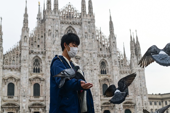 Un touriste portant un masque respiratoire donne de la nourriture aux pigeons sur la Piazza Duomo de Milan, le 5 mars 2020. (Photo : PIERO CRUCIATTI/AFP via Getty Images)