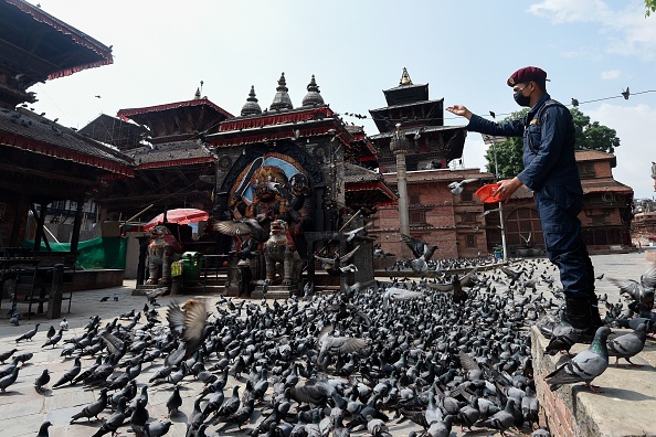 -Un membre de la police népalaise nourrit des pigeons sur la place Durbar lors d'un verrouillage national imposé par le gouvernement à titre de mesure préventive contre le coronavirus COVID-19, à Katmandou le 16 avril 2020. Photo de PRAKASH MATHEMA / AFP) via Getty Images.