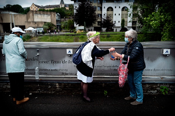 Des pèlerins collectent de l'eau avec l'aide d'un bénévole au sanctuaire de Notre-Dame de Lourdes à Lourdes. (Photo : LIONEL BONAVENTURE/AFP via Getty Images)