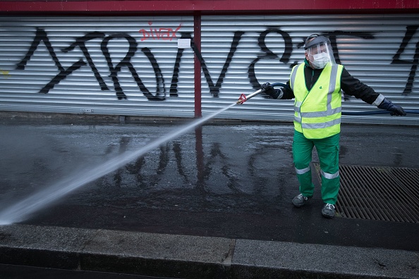 Un ouvrier du service de nettoyage de la municipalité de Paris "Proprete de Paris", portant un équipement de protection, nettoie un trottoir avec un tuyau d'arrosage à Paris, le 29 avril 2020. (JOEL SAGET/AFP via Getty Images)