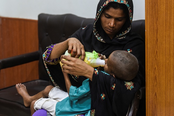 Une mère nourrit son fils séropositif en attendant son tour dans un centre de soutien au traitement du VIH au Pakistan, le 25 mars 2021. Photo par Asif HASSAN / AFP via Getty Images.