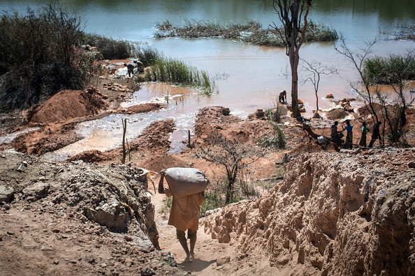 -Près d'une mine entre Lubumbashi et Kolwezi en RDC montre un homme portant un sac de minéraux alors que des gens séparent le cobalt du sable et de la roche dans un lac. Photo FEDERICO SCOPPA/AFP via Getty Images.