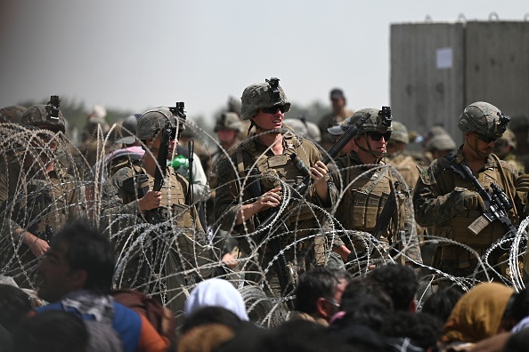 Des soldats américains montent la garde derrière des barbelés alors que des Afghans sont assis au bord d'une route près de la partie militaire de l'aéroport de Kaboul le 20 août 2021. Photo Wakil KOHSAR / AFP via Getty Images.