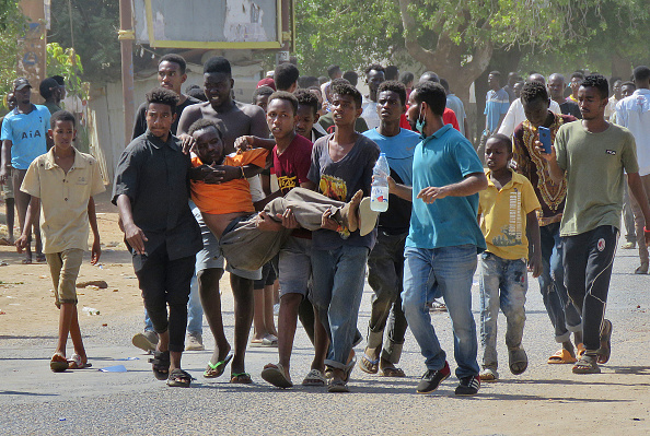 Des Soudanais transportent un homme blessé lors d'affrontements dans le cadre de manifestations contre un coup d'État militaire qui a renversé la transition vers un régime civil, le 25 octobre 2021 dans la capitale Khartoum. Photo by -/AFP via Getty Images.