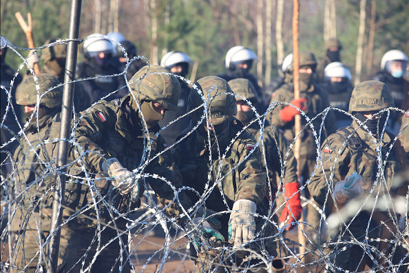 Le personnel de sécurité polonais derrière une clôture de barbelés à la frontière biélorusse-polonaise où des milliers de migrants se sont rassemblés dans le but d'entrer en Pologne, membre de l'UE.  (Photo : LEONID SHCHEGLOV/BELTA/AFP via Getty Images)