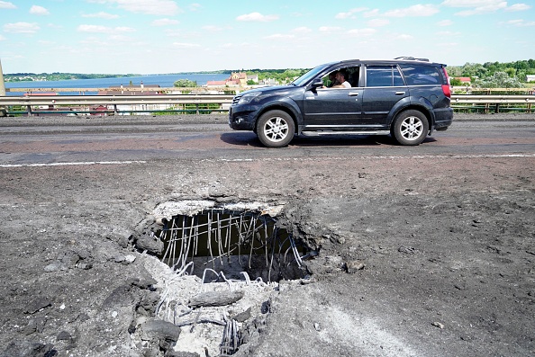 Une voiture passe devant un cratère sur le pont Antonovsky de Kherson sur le fleuve Dnipro causé par une frappe de roquette le 21 juillet 2022. Photo par STRINGER/AFP via Getty Images.