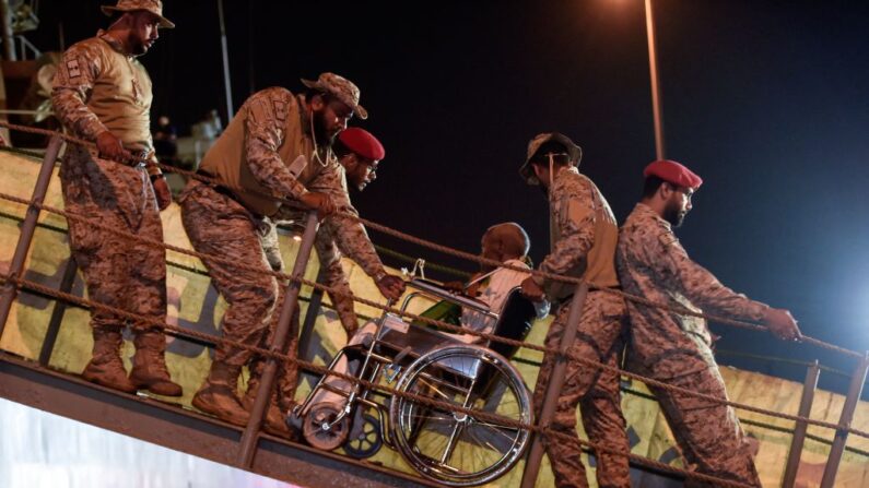 Le personnel de la marine saoudienne aident un homme en fauteuil roulant à évacuer du Soudan à son arrivée à la base navale du Roi Faisal à Jeddah, le 26 avril 2023. (AMER HILABI/AFP via Getty Images)