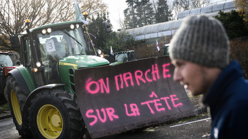 Un agriculteur conduit son tracteur en arborant une pancarte signifiant "On marche sur la tête" lors d'une manifestation des principaux syndicats français pour protester contre la politique agricole, devant le Conseil général de Bretagne à Rennes, dans l'ouest de la France, le 6 décembre 2023. (LOIC VENANCE/AFP via Getty Images)