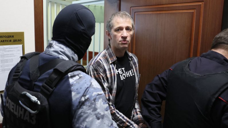 Menotté, le journaliste russe Roman Ivanov (au c.) portant un T-shirt sur lequel on peut lire "Pas de guerre" est escorté par les forces de l'ordre russes, le 6 mars 2024. (Photo STRINGER/AFP via Getty Images)