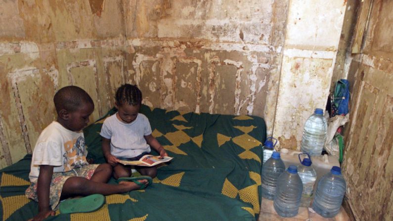 Two children read a comic strip in their room with damp moldy walls, on July 3, 2001 in Paris, rue Mont-Cenis in the 18th arrondissement, in this unsanitary building which should soon be destroyed. In the absence of running water, water bottles are stored in the room. (Photo by Jack GUEZ / AFP) (Photo by JACK GUEZ/AFP via Getty Images)