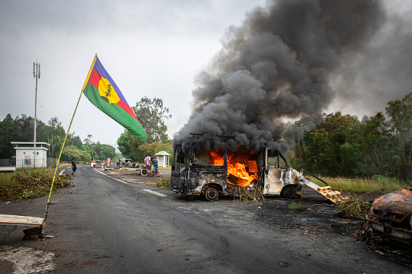 Un drapeau kanak flottant à côté d'un véhicule en feu à un barrage routier indépendantiste à La Tamoa, dans la commune de Paita, en Nouvelle-Calédonie. (Photo DELPHINE MAYEUR/AFP via Getty Images)