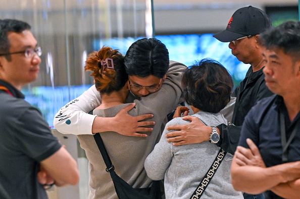 Les passagers du vol Singapore Airlines reliant Londres à Singapour, qui a effectué un atterrissage d'urgence à Bangkok, saluent les membres de leur famille à leur arrivée à l'aéroport de Changi à Singapour, le 22 mai 2024. (Photo ROSLAN RAHMAN/AFP via Getty Images)