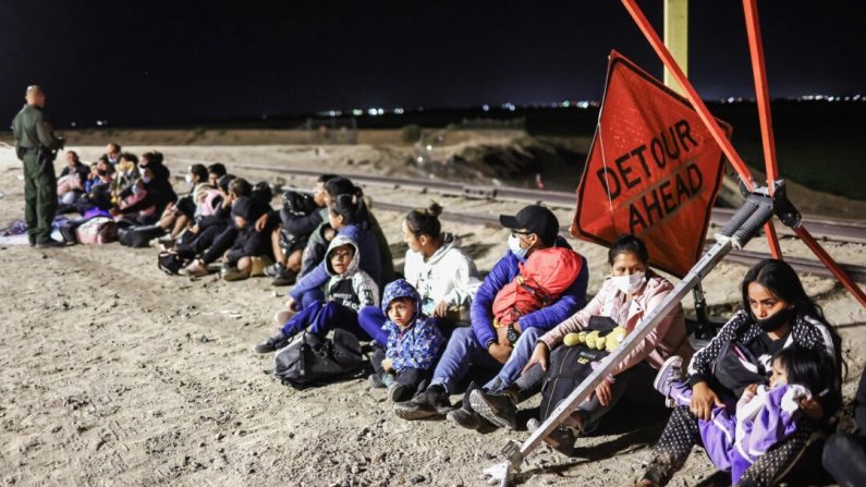 Des immigrés clandestins attendent de passer devant les agents de la patrouille frontalière après avoir traversé le Mexique. En arrière-plan, la barrière frontalière entre les États-Unis et le Mexique à Yuma, en Arizona, le 23 mai 2022. (Mario Tama/Getty Images)