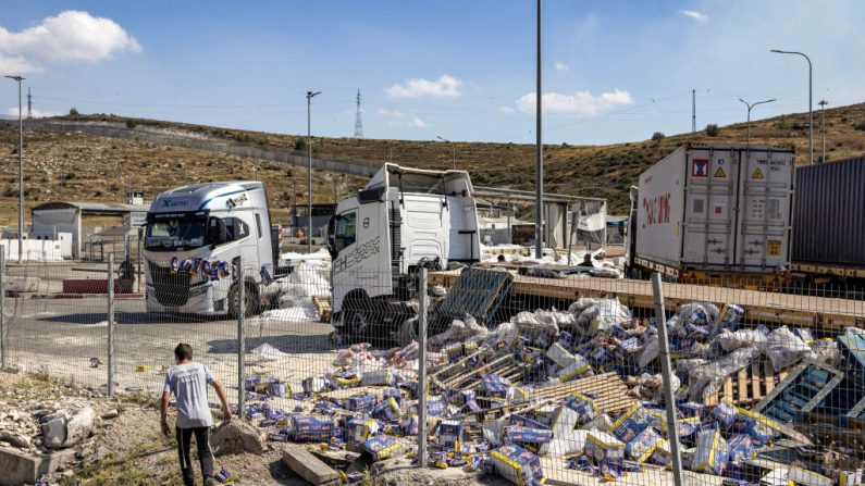 Un jeune marche près des camions remorques endommagés qui transportaient de l'aide humanitaire du côté israélien du point de passage de Tarqumiyah avec la Cisjordanie occupée, le 13 mai 2024, après qu'ils ont été vandalisés par des activistes israéliens. (OREN ZIV/AFP via Getty Images)