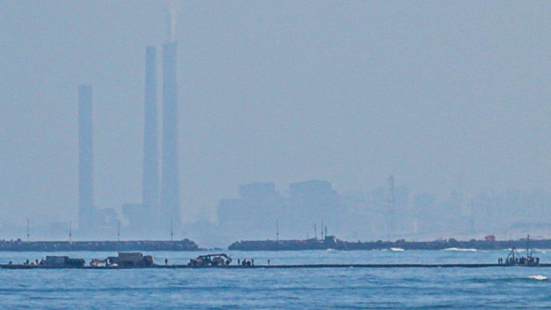 Cette photo prise le 16 mai 2024 montre la jetée temporaire Trident Pier construite par les Etats-Unis et reliée au littoral de Gaza afin d'accélérer l'aide humanitaire d'urgence au territoire palestinien ravagé par la guerre, et à l'arrière-plan une vue de la centrale électrique israélienne Rutenberg près de la ville israélienne d'Ashkelon. (AFP via Getty Images)