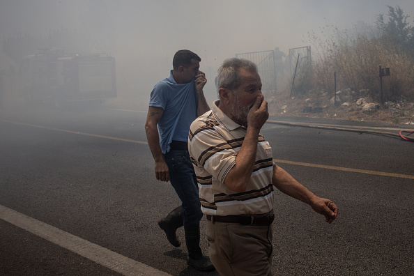 Des civils se couvrent le visage de la fumée causée par les multiples frappes israéliennes qui ont touché des cibles près de la route principale de la ville, le 26 juin 2024 à Bint Jbeil, au Liban. (Chris McGrath/Getty Images)