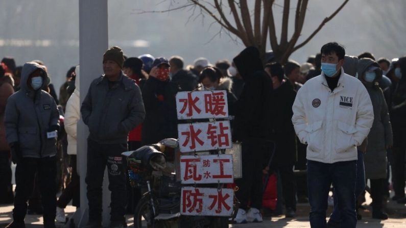 Des travailleurs migrants attendent dans une rue d'être embauchés, à côté de panneaux annonçant leurs compétences, à Shenyang, dans la province de Liaoning, en Chine, le 6 février 2023. (STR/AFP via Getty Images)