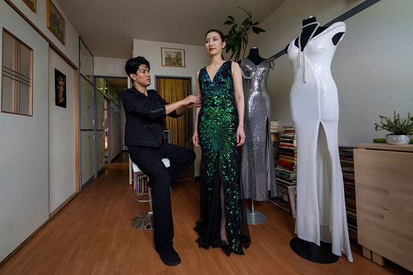 Cette photo prise le 23 mai 2024 montre le créateur de mode Shibuya Zarny (à gauche), né au Myanmar, en train de vérifier l'ajustement d'une robe sur un mannequin dans son atelier de Tokyo. Après avoir fui le Myanmar pour le Japon avec ses parents lorsqu'il était enfant, Shibuya Zarny a commencé sa carrière dans la mode en tant que mannequin à Tokyo, avant de confectionner des vêtements pour la royauté. (Photo KAZUHIRO NOGI/AFP via Getty Images) 

