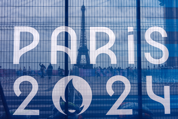 Des touristes regardent la Tour Eiffel derrière une barrière de sécurité avec une bannière avec le signe des Jeux olympiques de Paris 2024 au Trocadéro à Paris le 8 juillet 2024, avant les prochains Jeux olympiques de Paris 2024. (Photo  DIMITAR DILKOFF/AFP via Getty Images)