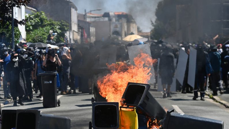 Des manifestants se tiennent derrière une barricade de déchets en feu lors d'une manifestation contre la construction de méga-bassine à La Rochelle, le 20 juillet 2024. (Crédit photo CHRISTOPHE ARCHAMBAULT/AFP via Getty Images)
